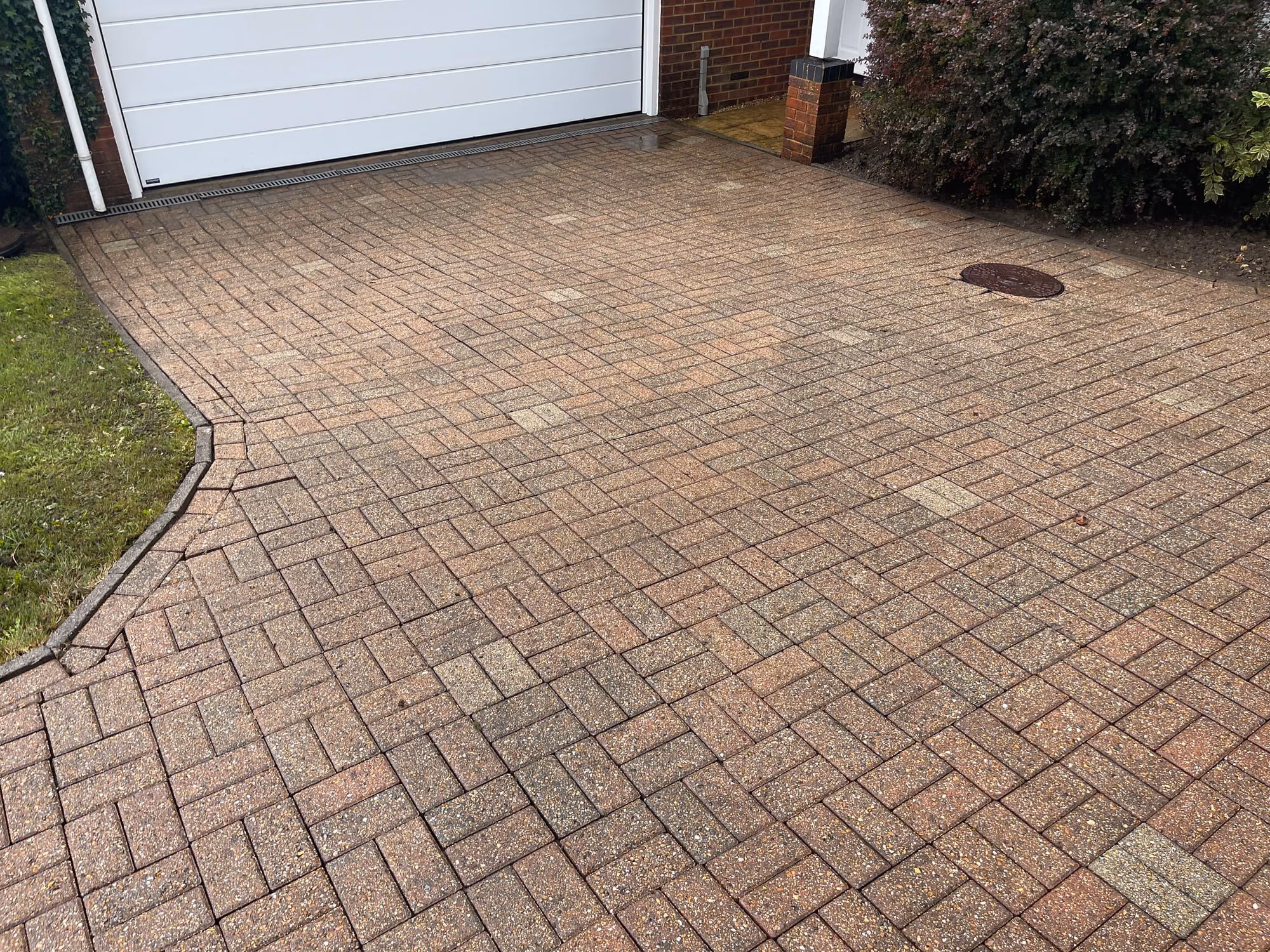 Block paved driveway in front of a white up-and-over garage door, laid in herringbone with a curved edging course and a drain cover set into it