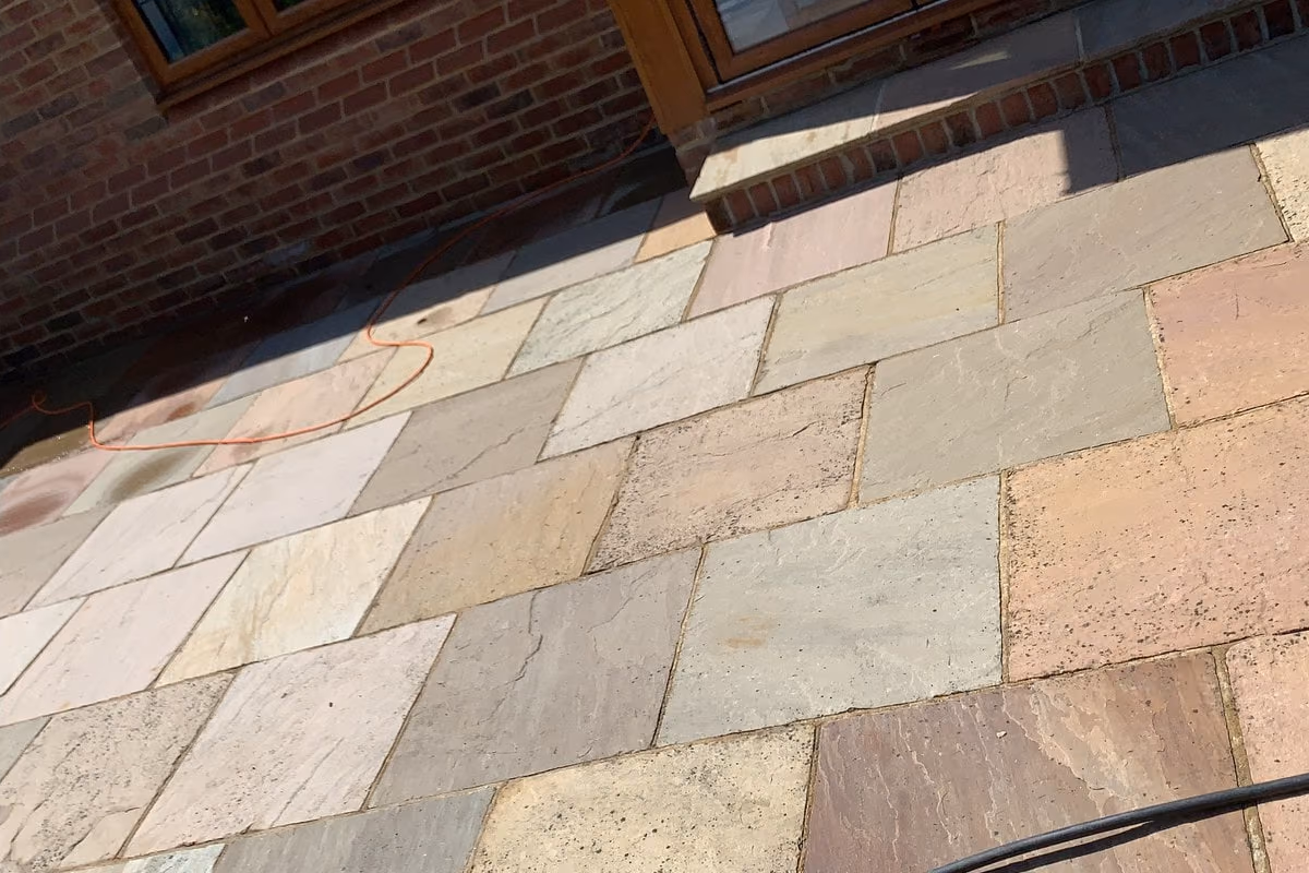 Cleaned Indian sandstone paving photographed close up, the buff, pink and grey variation between slabs visible again and the joints clear