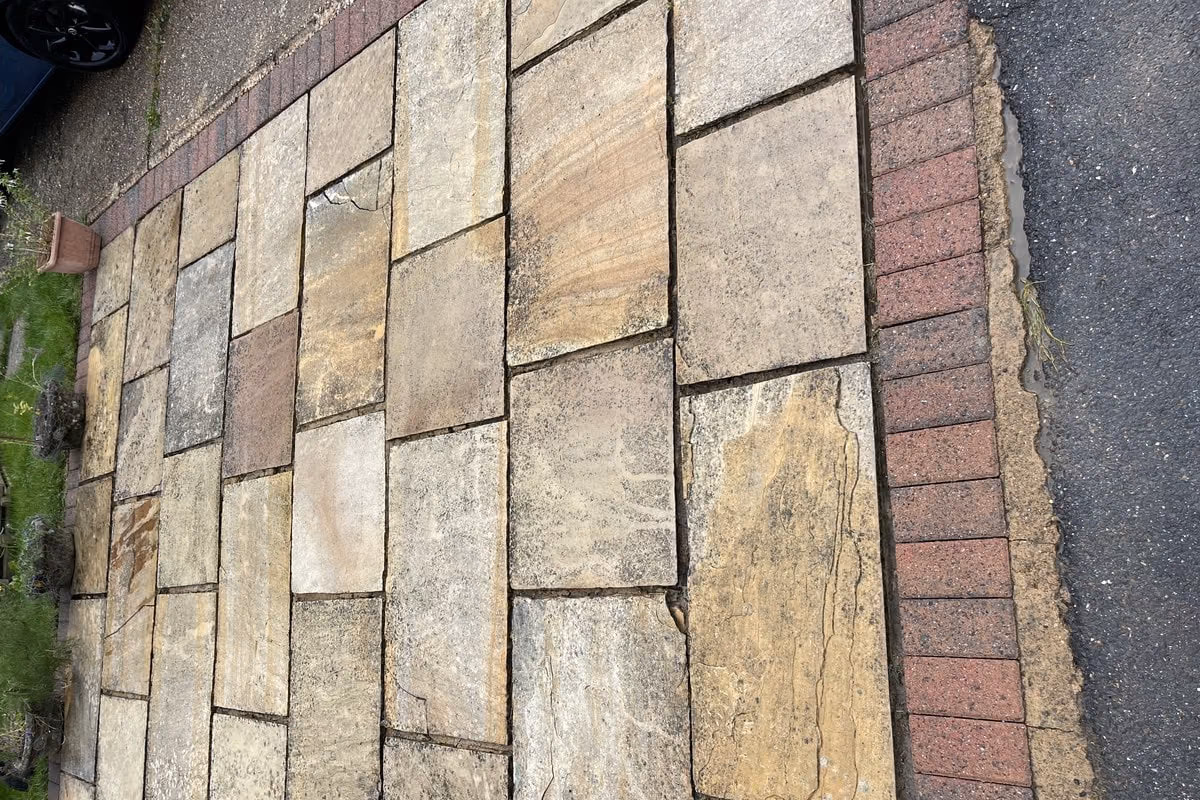 The same run of sandstone flags after cleaning, each slab a different shade of buff and rust, with the brick edging clear