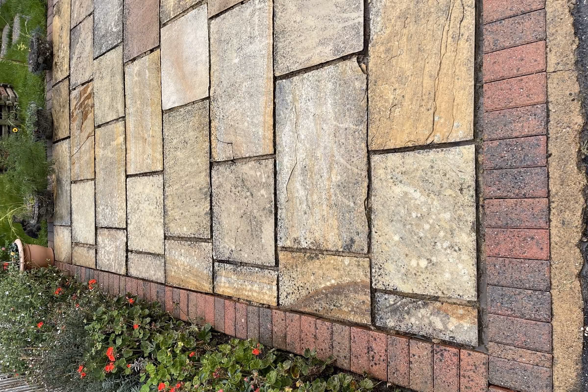 The cleaned sandstone paving close up, warm buff and rust tones showing through, with the brick edging and a planted border alongside